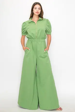 A woman in green jumpsuit standing on white background.